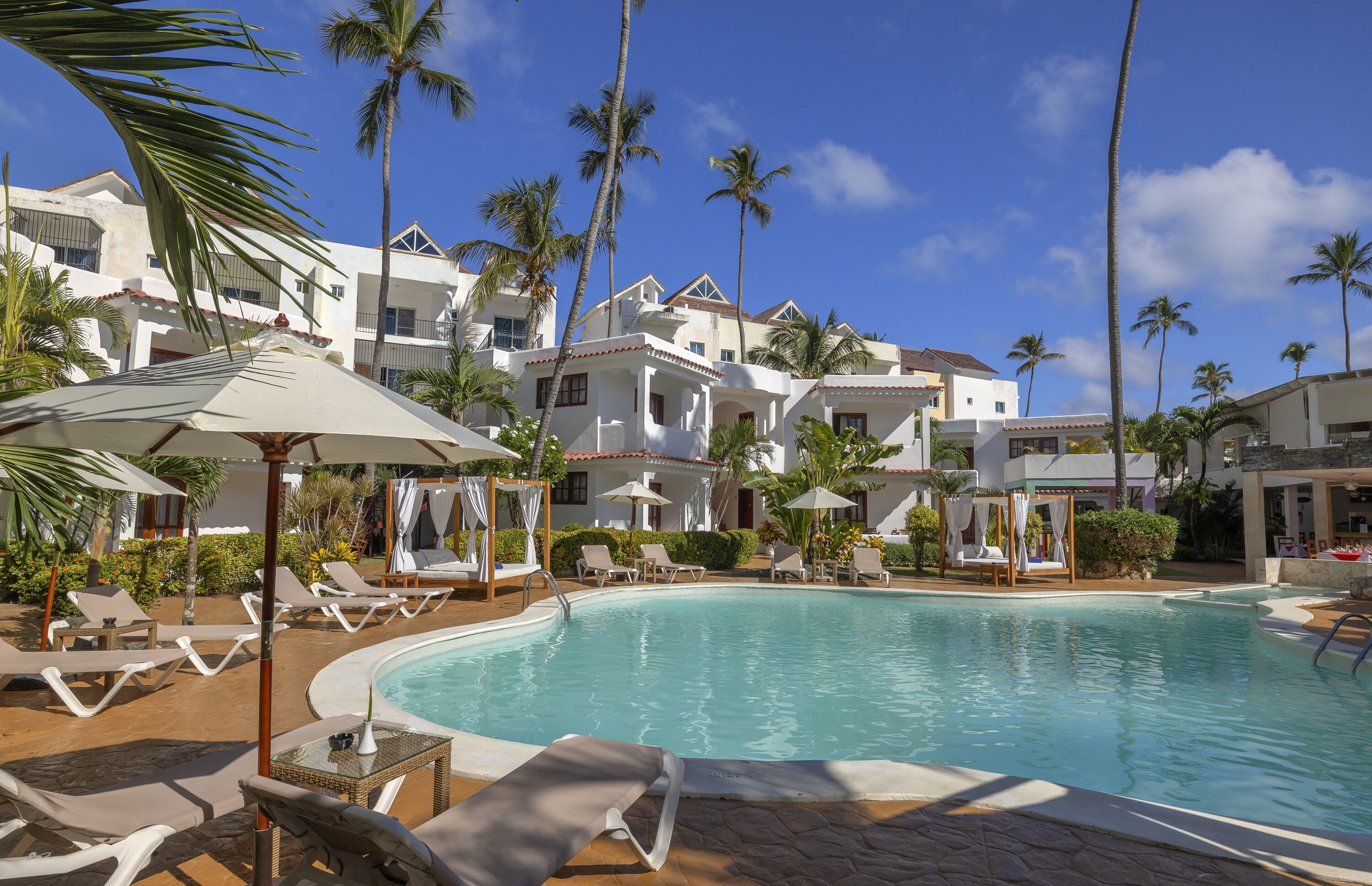 Un espace aménagé au bord de la piscine, avec des chaises longues, des parasols et une piscine à l’eau d’un bleu limpide.