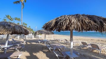 Una playa con sombrillas de paja y sillas de descanso.