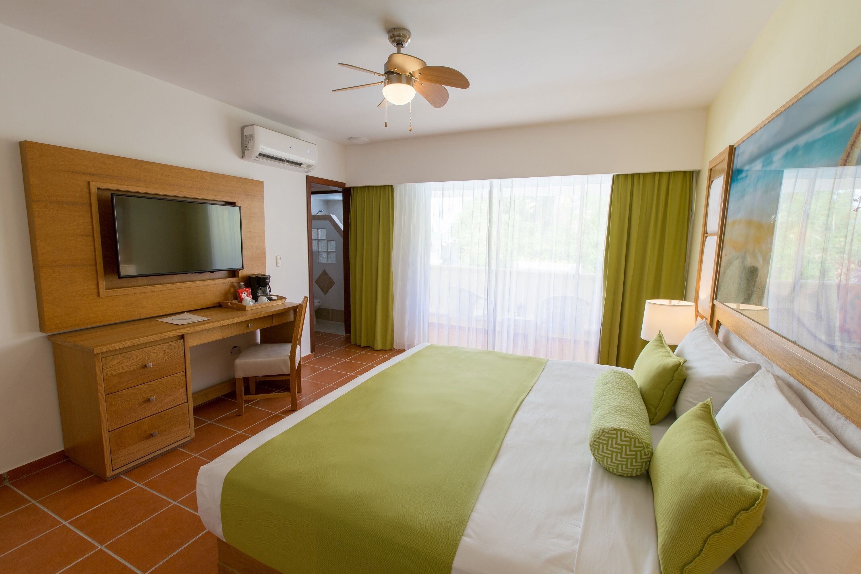 Una camera d'albergo con un letto, una scrivania, una televisione e una ventola a soffitto.