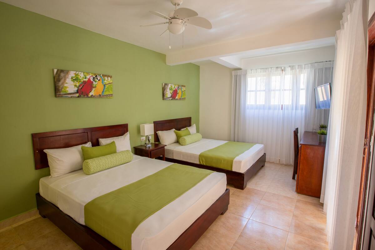 A hotel room with two beds, green walls, and artwork.