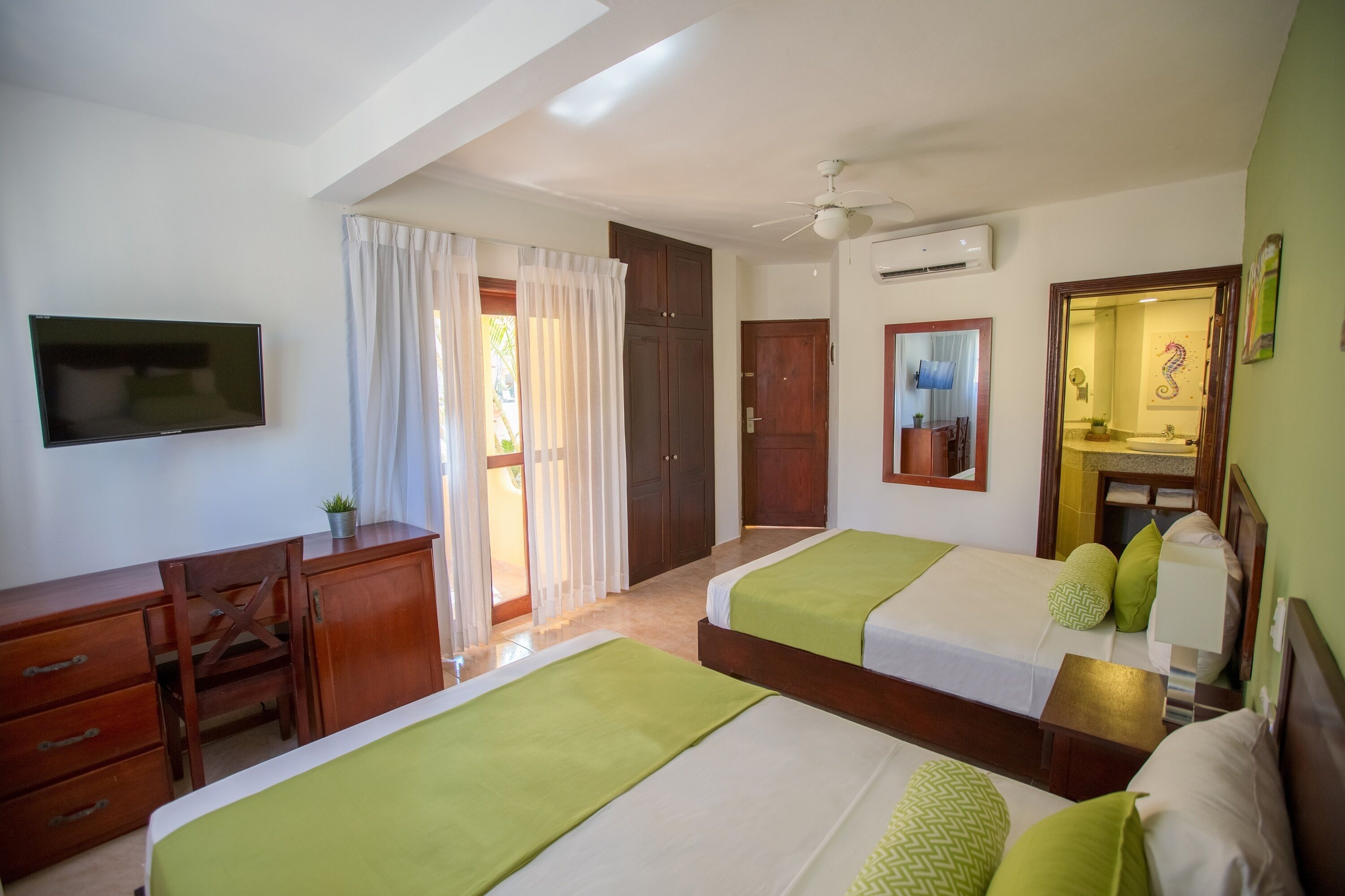 A hotel room with two beds, a desk, a TV, and a bathroom visible through an open door.