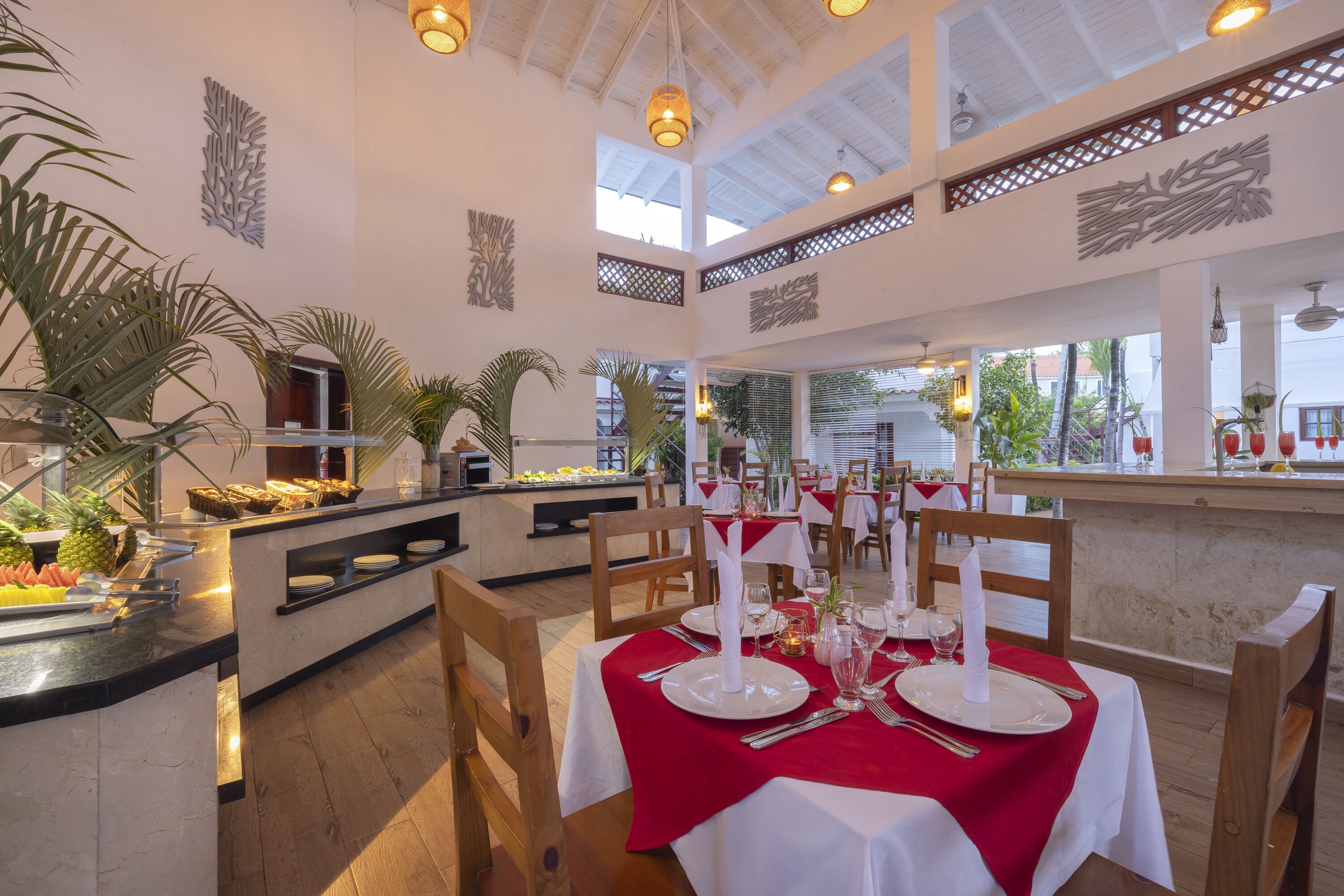 Un restaurant avec un plafond haut, des chaises en bois et des tables recouvertes de nappes blanches et agrémentées de serviettes rouges.