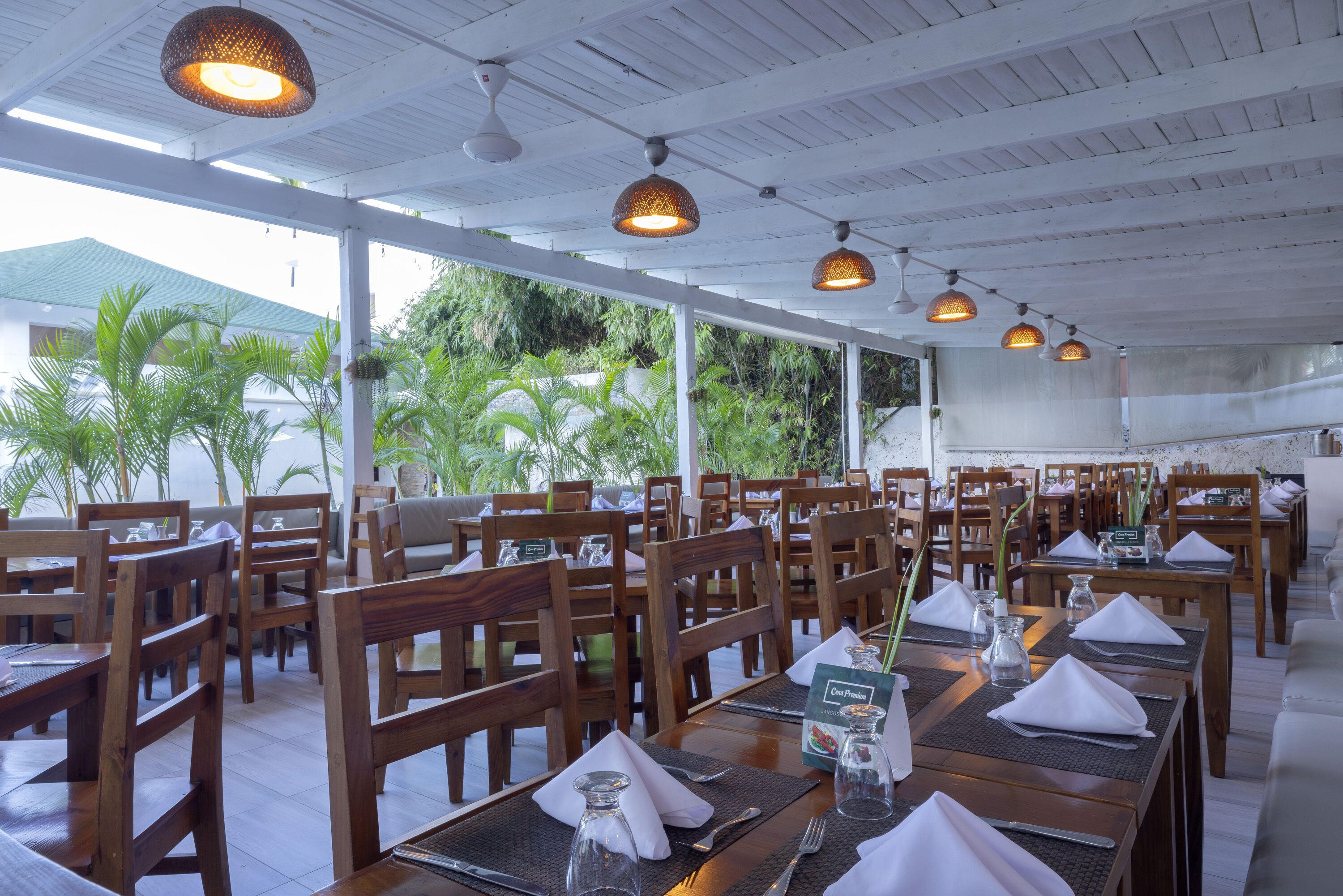 A restaurant with wooden tables and chairs, large windows, and hanging pendant lights.