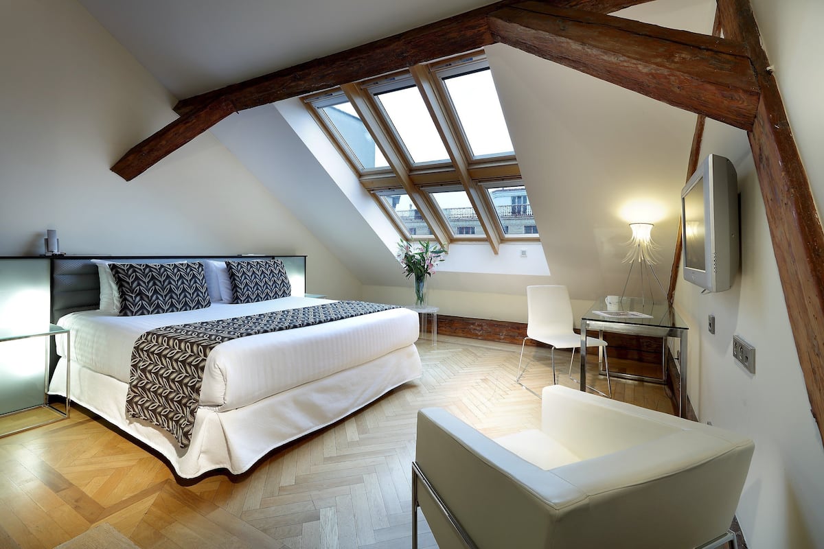 A bedroom with a bed, a chair, a desk, and a TV.