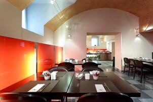 Een moderne eetruimte met tafels en stoelen, een keuken op de achtergrond, en een hoog plafond met zichtbare balken.