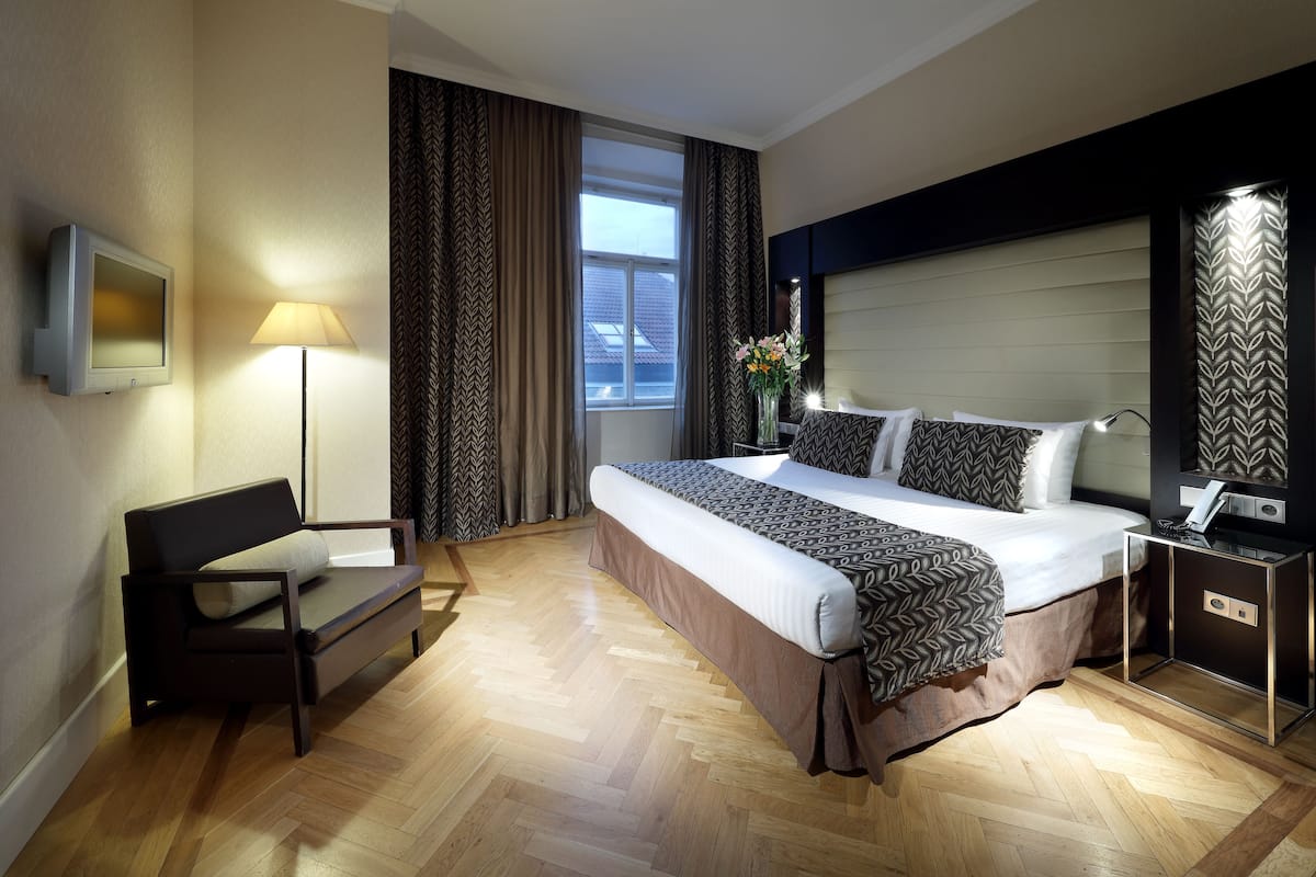A hotel room with a bed, a sofa, a desk, a lamp, and a TV.