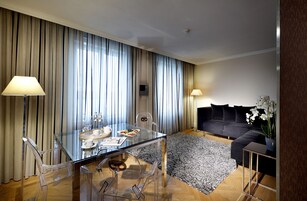 Uma sala de estar moderna com uma mesa de jantar de vidro, cadeiras transparentes, um sofá preto e um tapete estampado.