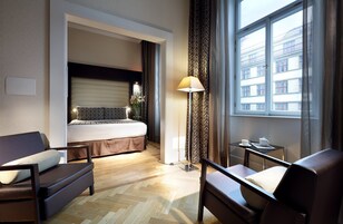 Quarto de hotel com cama, sofá, escrivaninha e luminária.