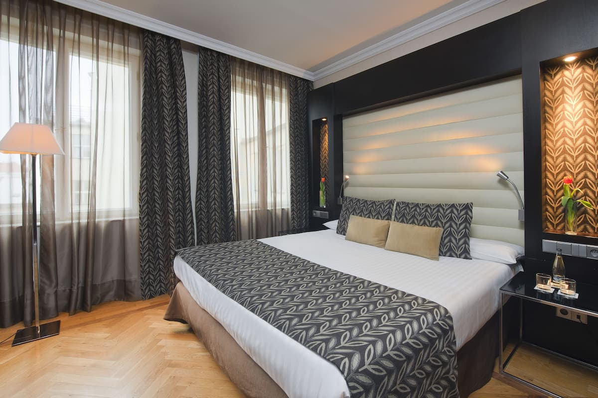 A modern hotel room with a large bed, a bedside table with a lamp, and a decorative wall panel.