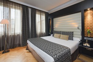 Quarto de hotel moderno com uma cama grande, uma mesinha de cabeceira com abajur e um painel decorativo na parede.