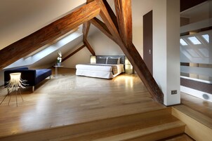 Quarto com teto inclinado, uma cama, mesa de cabeceira e abajur.