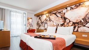 Hotellihuone, jossa on suuri sänky, työpöytä tietokoneella ja suuri abstrakti maalaus seinällä.