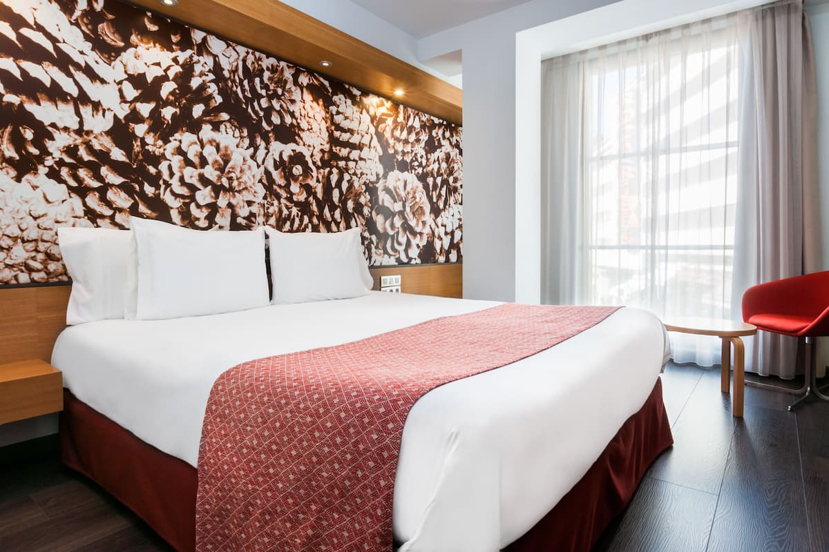 A hotel room with a large bed, a red chair, and a floral-patterned wall.