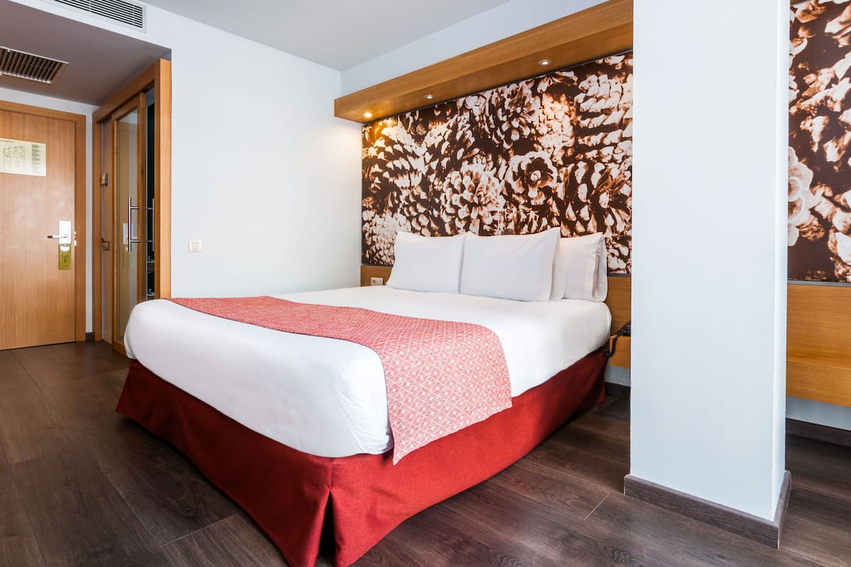 A hotel room with a large bed, a wooden headboard, and a floral-patterned wall.