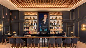 Una zona de bar con una barra larga, varios taburetes y estantes llenos de botellas.