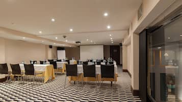 Un salón de conferencias con mesas y sillas, una pantalla para proyector y un suelo con diseño.