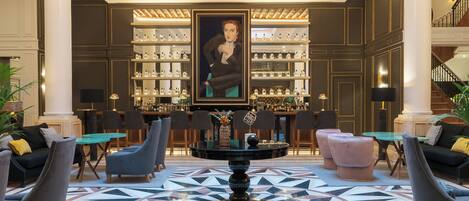 A lobby with a central round table, seating arrangements, a bar area, and a large portrait on the wall.