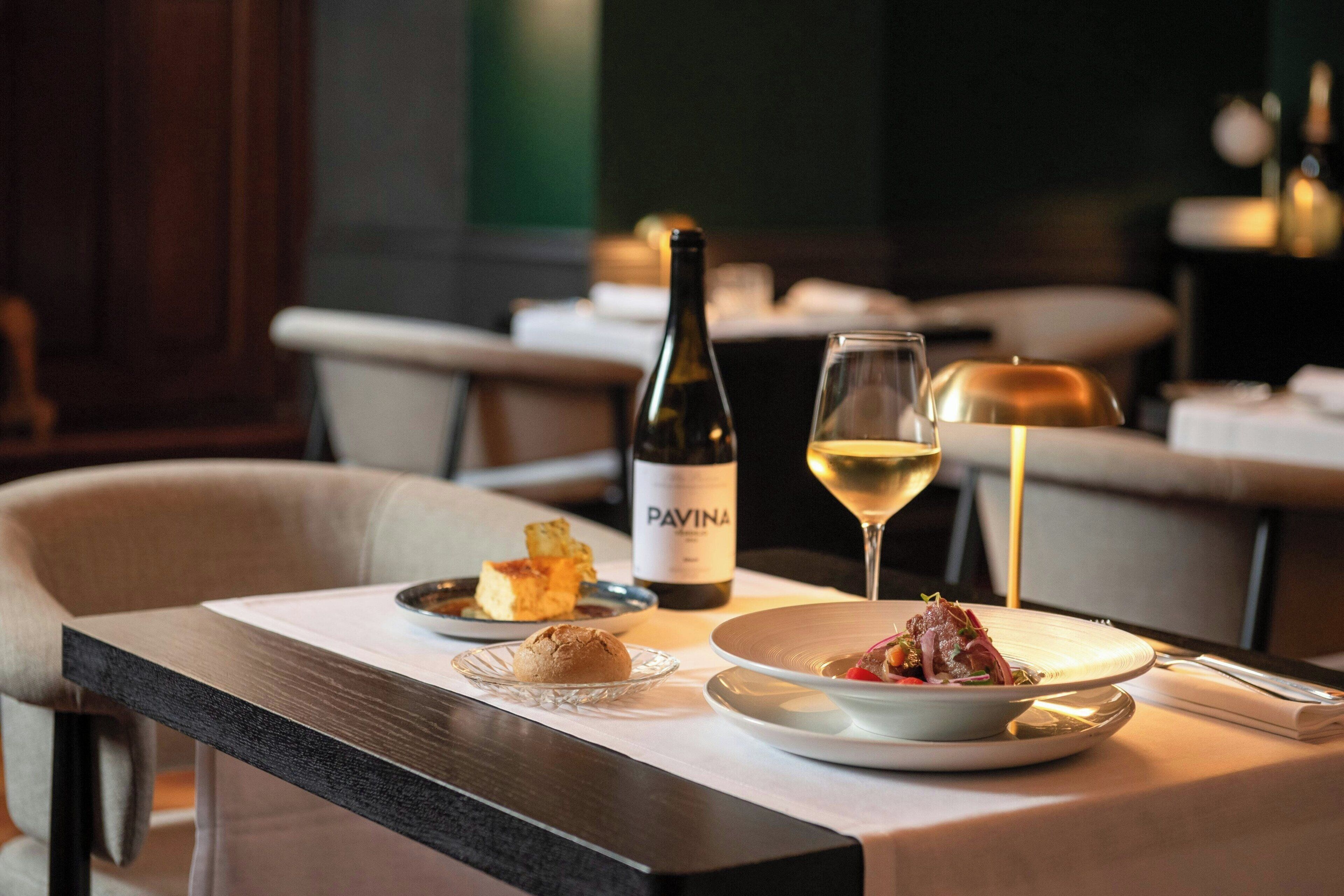 A dining table with a bottle of wine, a glass of wine, and plates of food.