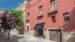 Un edificio rojo con toldo negro, una calle empedrada y un árbol de hojas moradas.