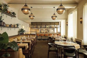 A restaurant with multiple dining tables, chairs, hanging pendant lights, and a kitchen area in the background. - Eurostars David (Prague)