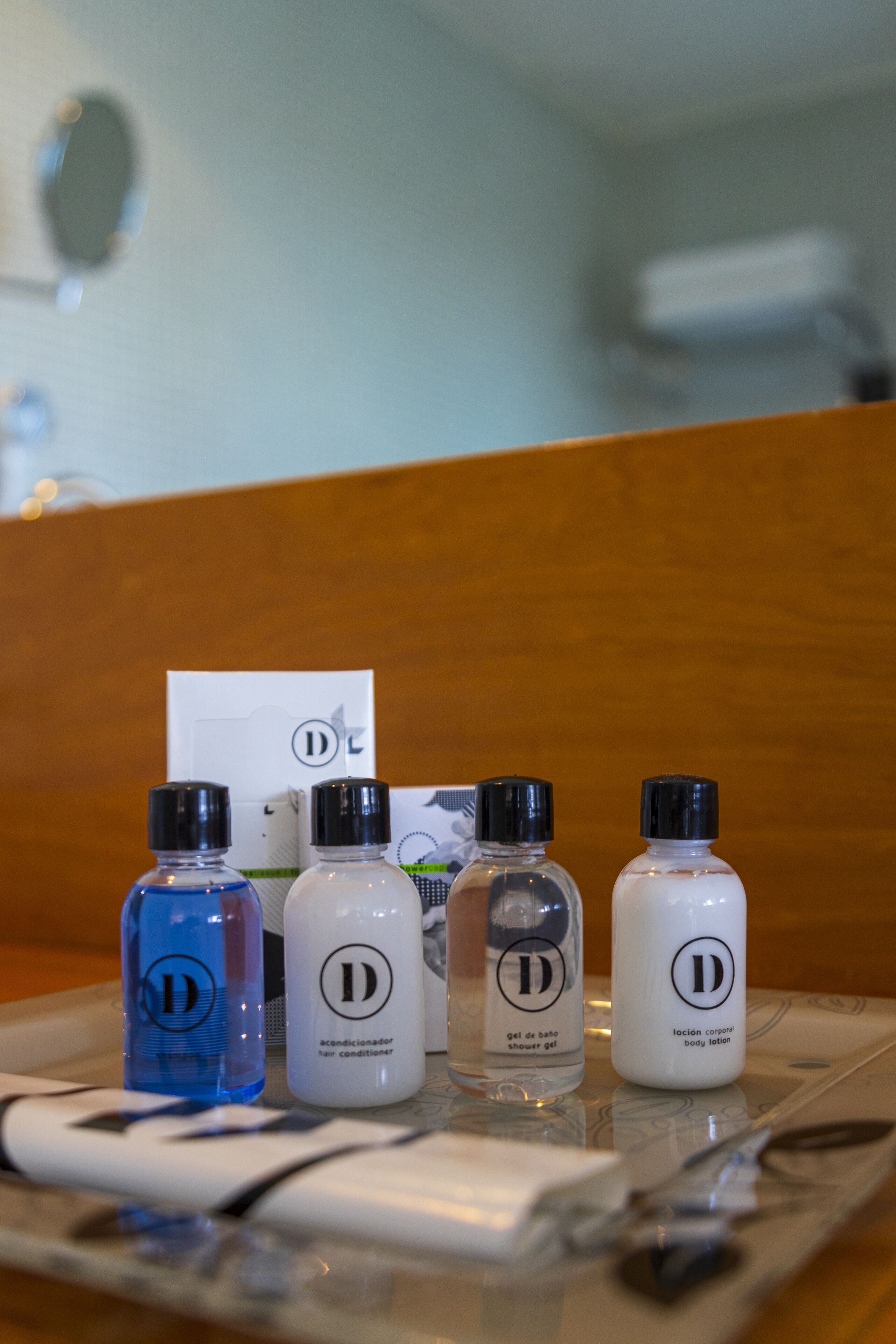 A tray with four bottles of toiletries and a card on a wooden surface.