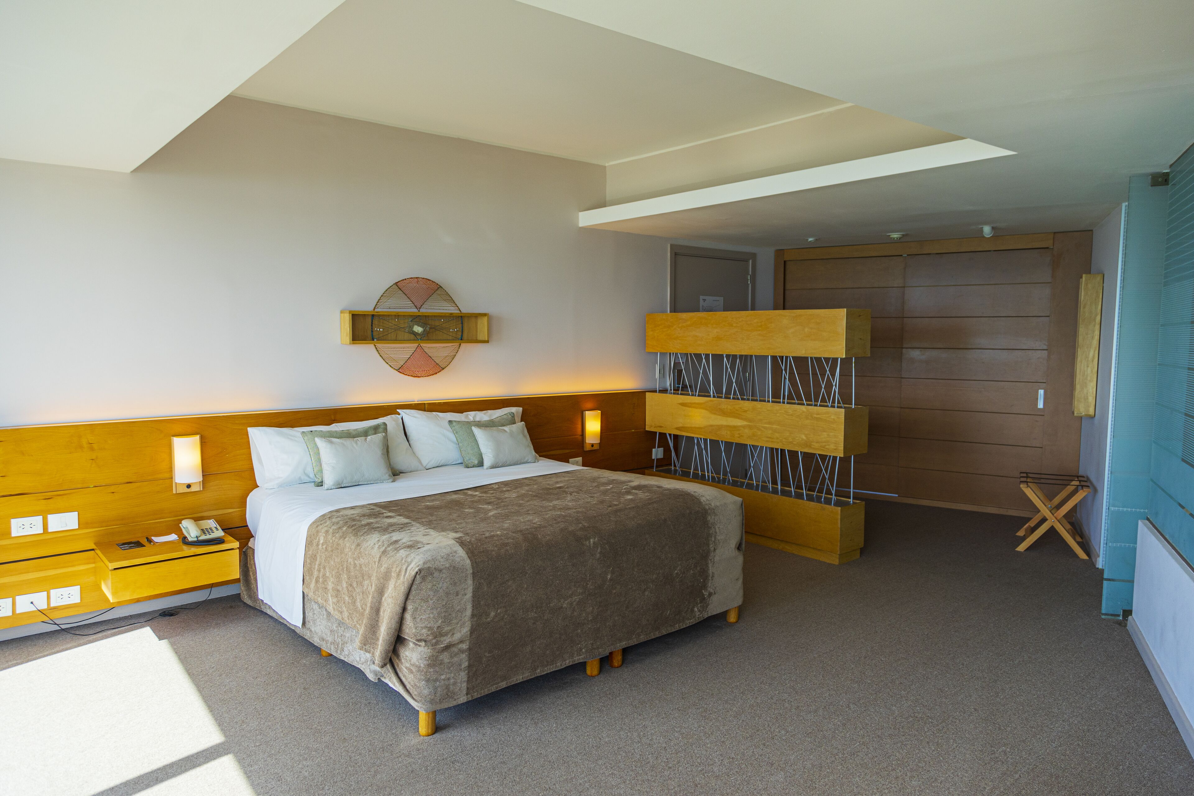 Un dormitorio con cama, mesitas de noche, lámpara de pared, cabecero de madera y una puerta.