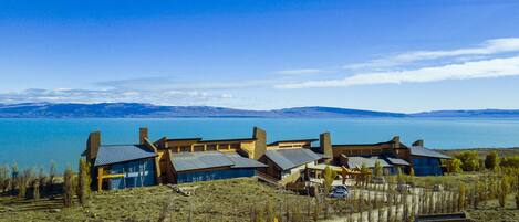 A lakeside property with multiple buildings, a dirt path, and a clear view of the lake and mountains in the background.