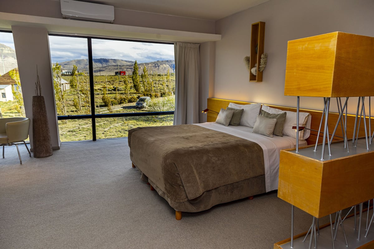 A modern bedroom with a large bed, a bedside table, and a view of a mountainous landscape through large windows.