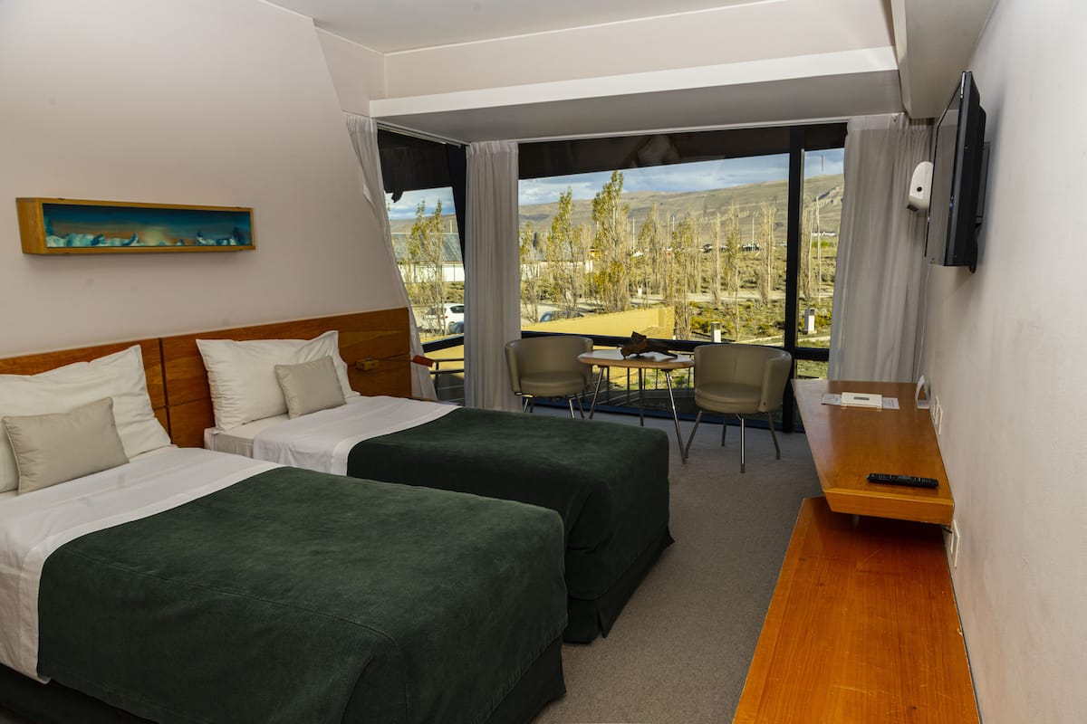 A hotel room with two beds, a desk, a chair, and a TV.