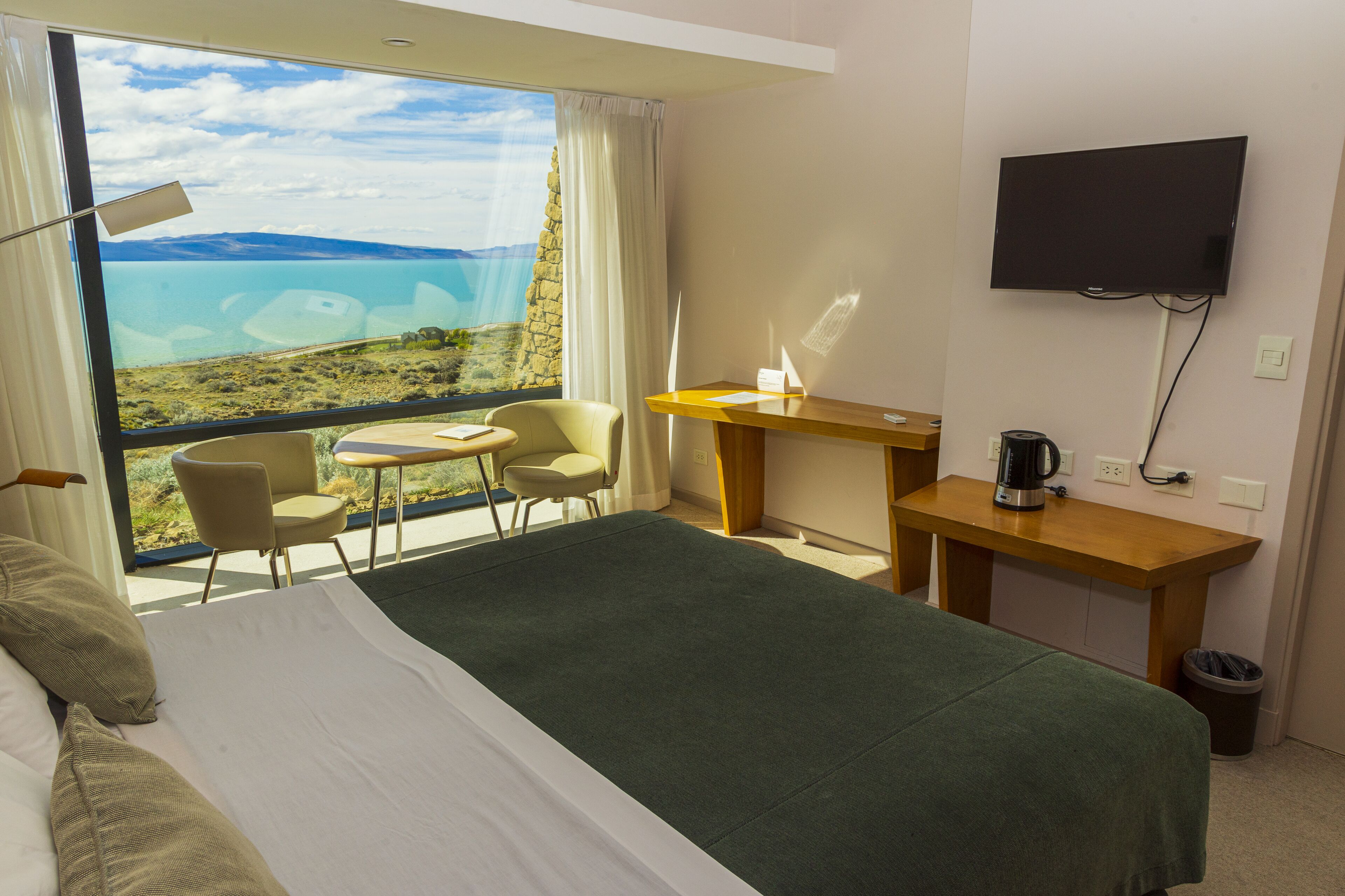 Ein Hotelzimmer mit Bett, Schreibtisch, Stuhl, Fernseher und Blick auf eine Landschaft.