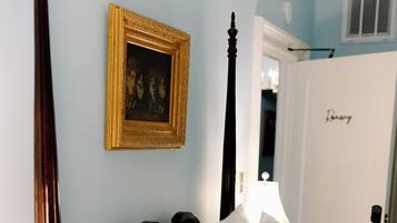 A bedroom with a four-poster bed, a bedside table with a lamp, and a framed picture on the wall.