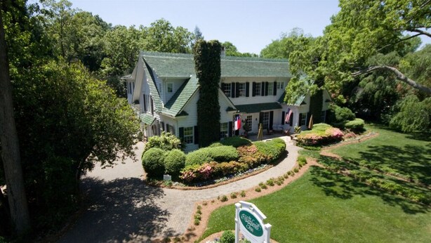 A large, two-story building with a green roof and white walls, surrounded by well-maintained gardens and a clear driveway.