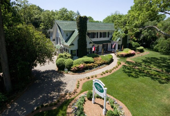 A large, two-story building with a green roof and white walls, surrounded by well-maintained gardens and a clear driveway. - Morehead Inn (Charlotte)
