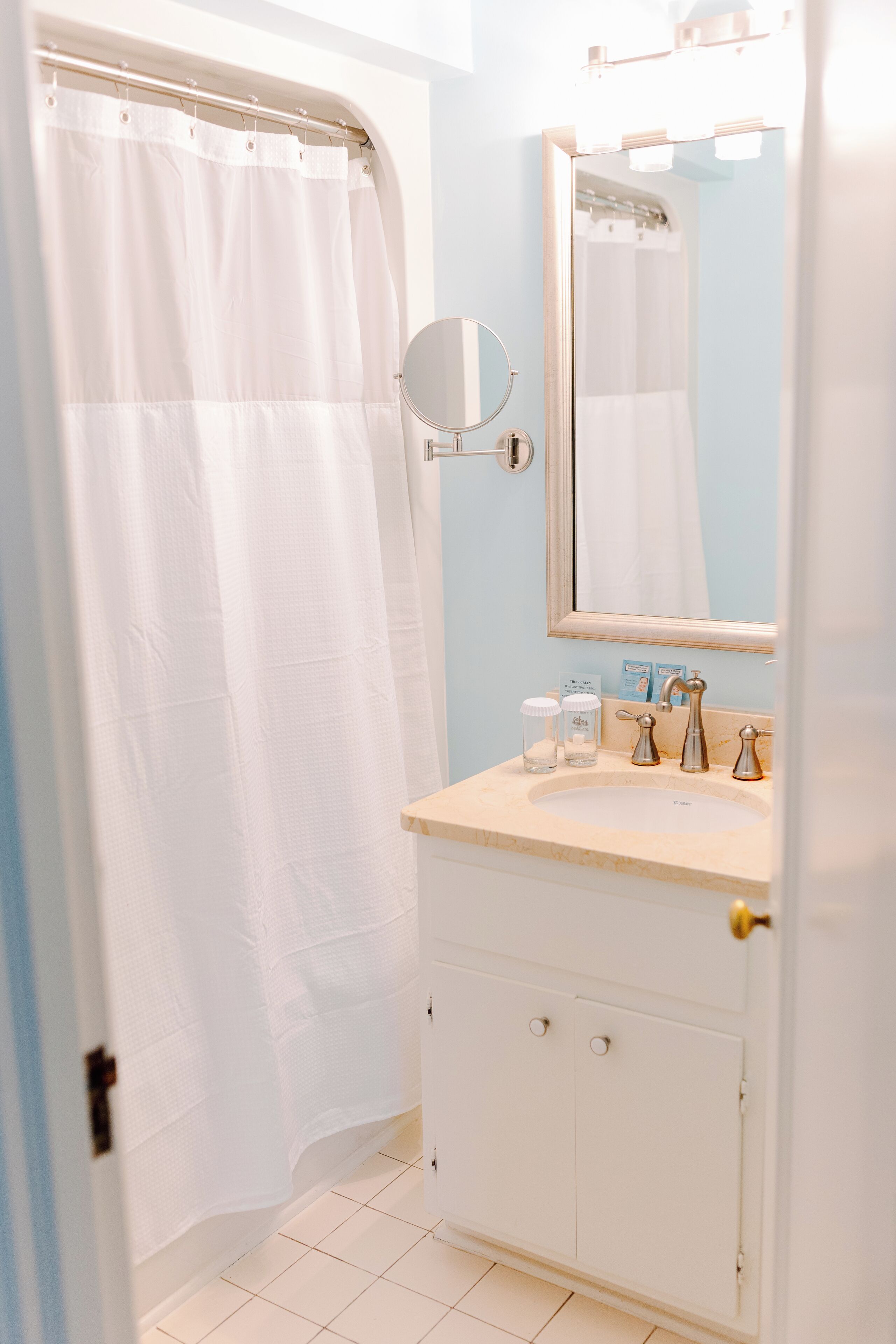 Een badkamer met een witte douchegordijn, een ronde spiegel, een wastafel met toiletartikelen en een kast.