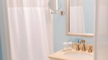 Een badkamer met een witte douchegordijn, een ronde spiegel, een wastafel met toiletartikelen en een kast.