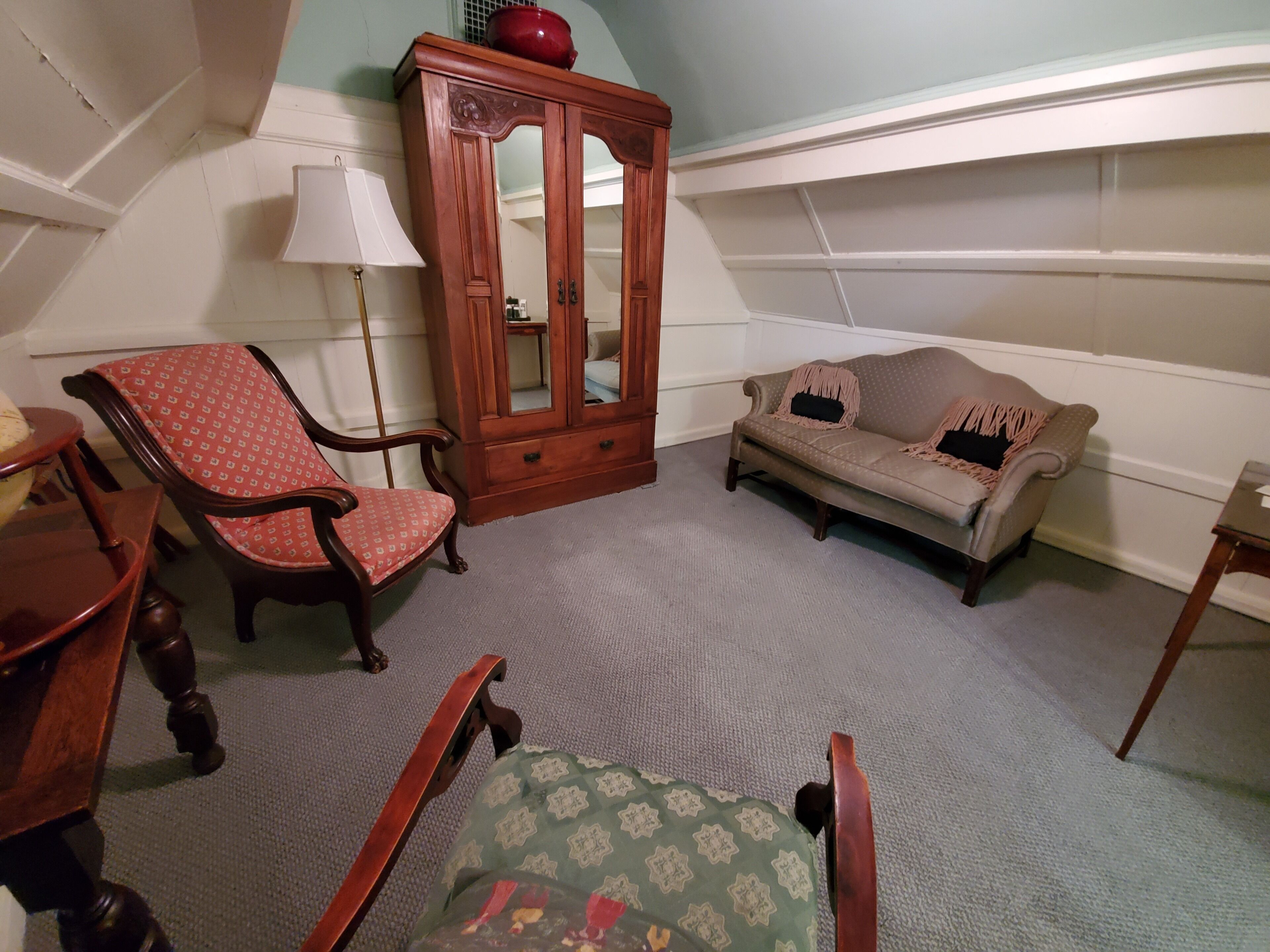 A room with a wooden cabinet, a red patterned chair, a beige sofa, and a green patterned chair.