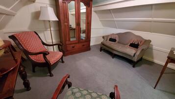 A room with a wooden cabinet, a red patterned chair, a beige sofa, and a green patterned chair.