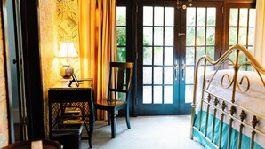 A bedroom with a bed, a chair, a desk with a lamp, and a door leading outside.