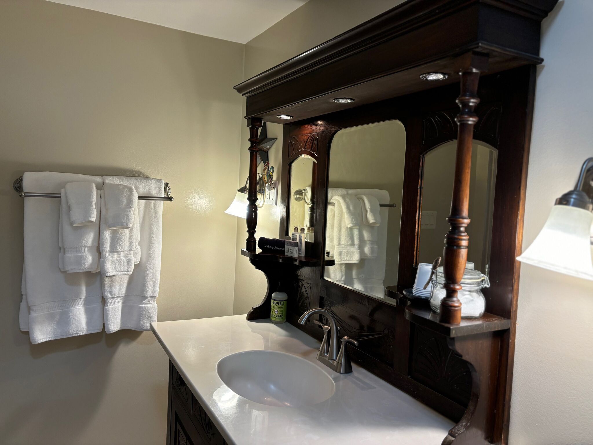 Une salle de bain avec un lavabo blanc, un grand miroir et un porte-serviettes sur lequel sont disposées plusieurs serviettes.