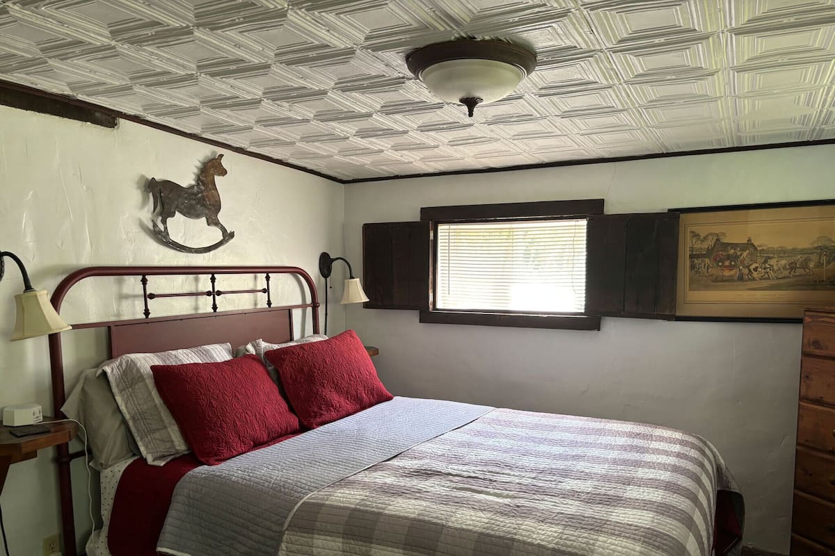 A bedroom with a bed, a window, a wall-mounted lamp, and a ceiling fan.