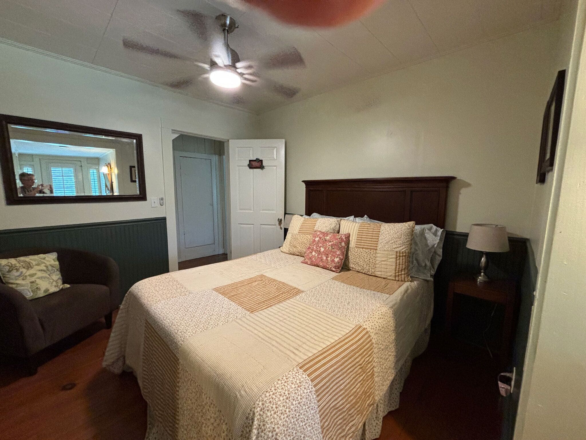 Un dormitorio con una cama, ventilador de techo, mesita de noche, lámpara, cómoda y espejo.