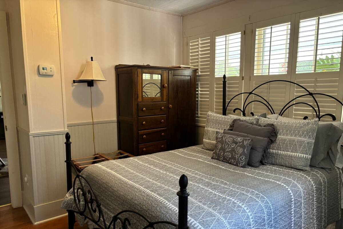 A bedroom with a bed, a dresser, a lamp, and a window with blinds.