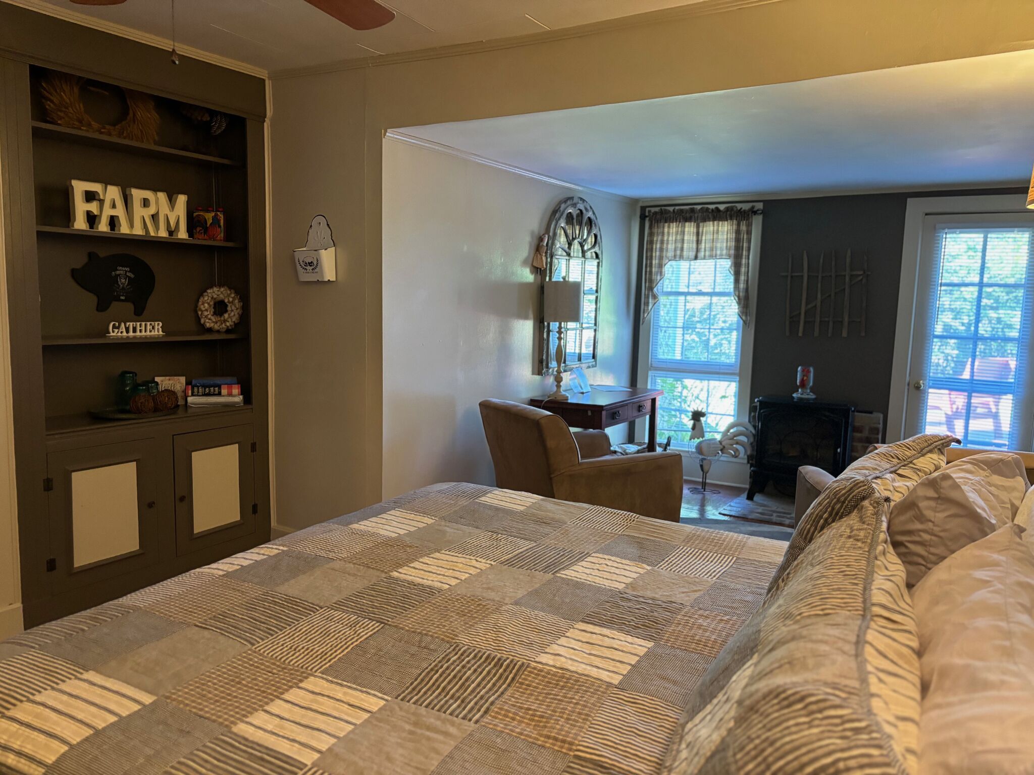 Un dormitorio con una cama grande, un armario de madera con letreros que dicen 'FARM' y 'GATHER', una silla, un escritorio y una ventana con cortinas.