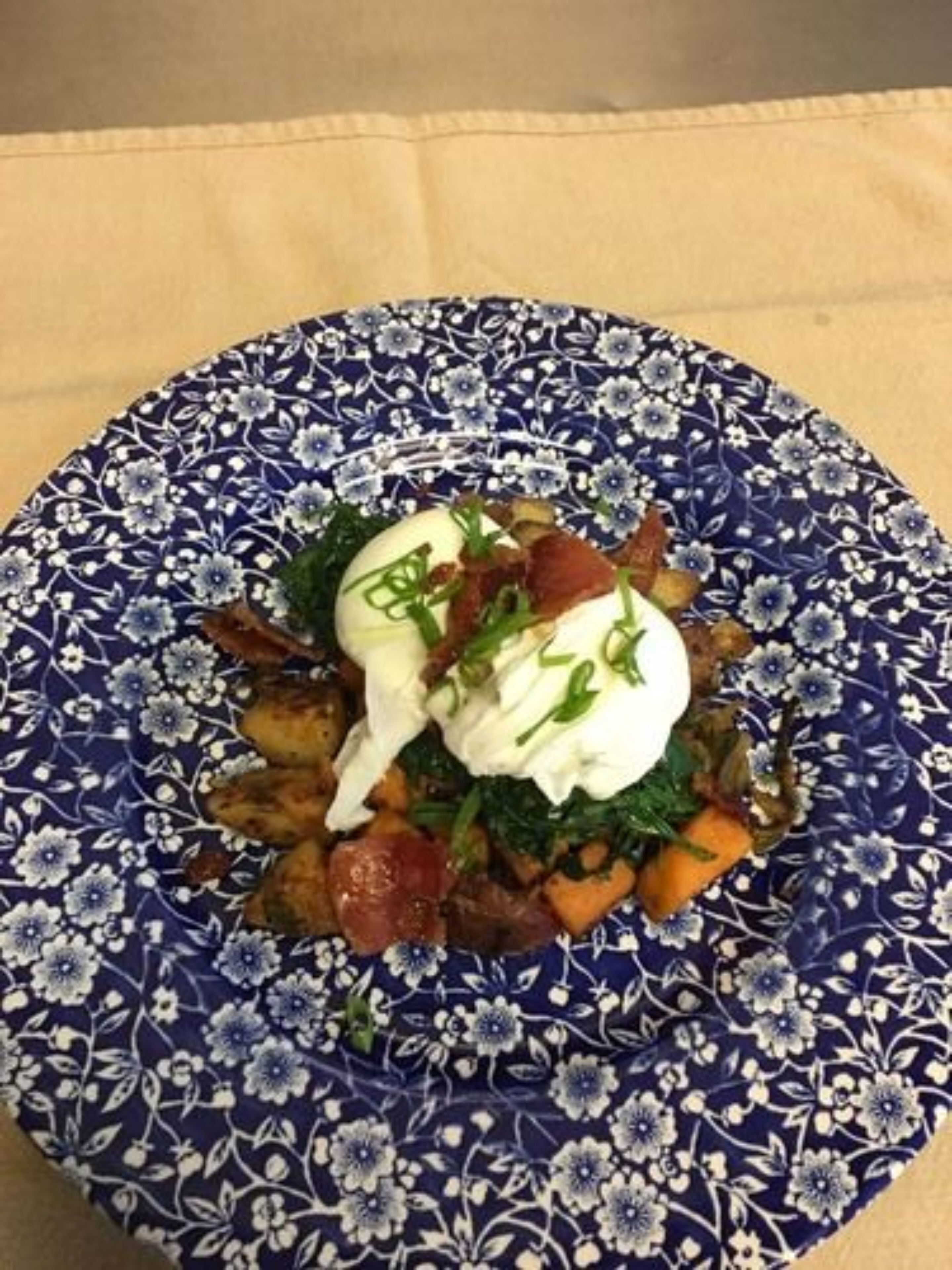 A plate of food with a blue floral pattern, including potatoes, greens, and a dollop of cream.