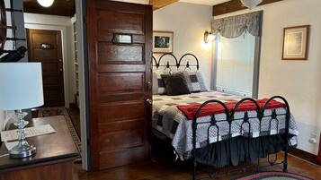 A bedroom with a wooden door, a bed with patterned bedding, a ceiling fan, and a window with blinds.
