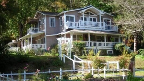 A two-story house with a front porch, a balcony on the upper floor, and a white picket fence.