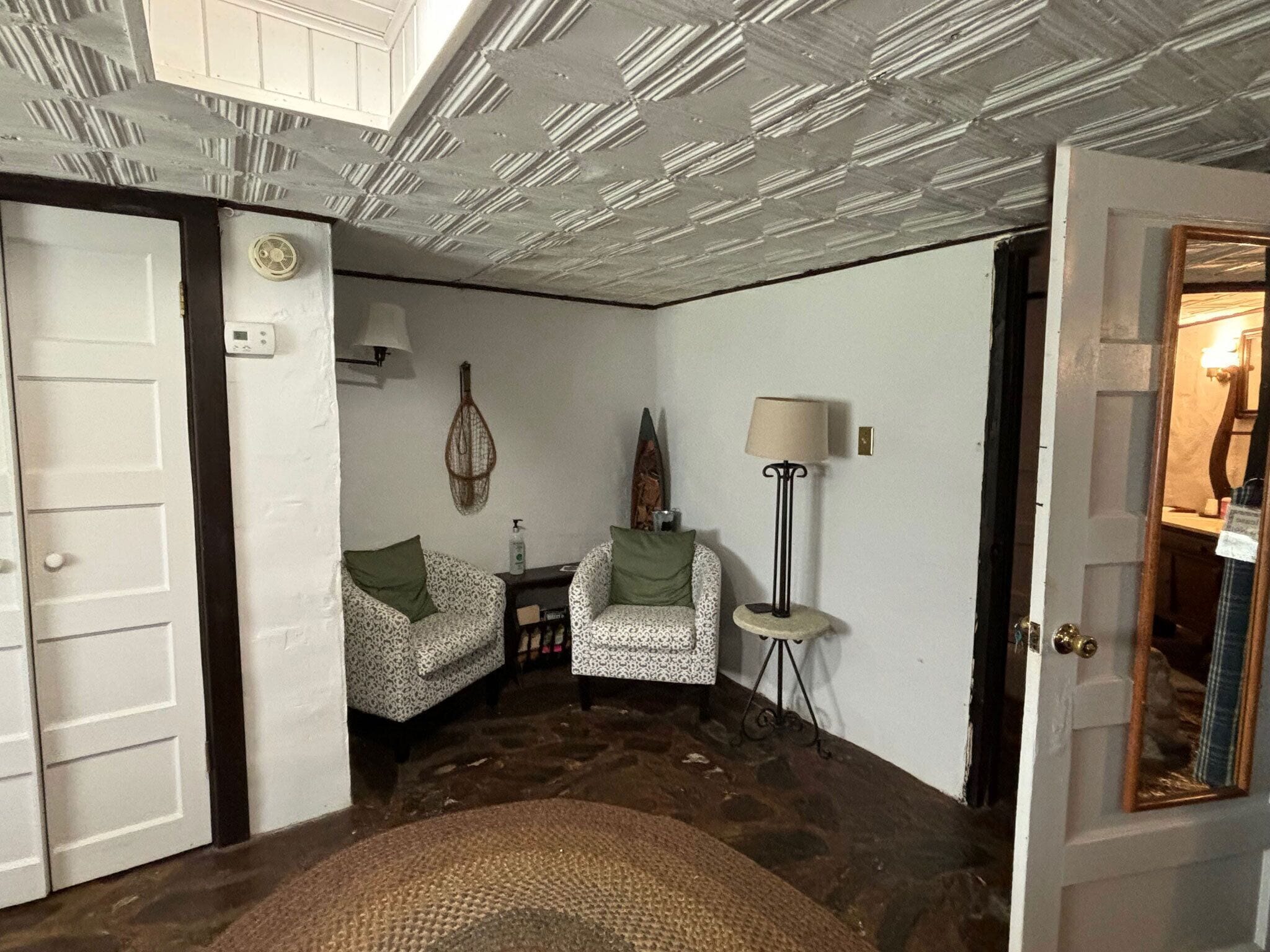 Quarto com sofá estampado, uma mesinha redonda, abajur e espelho na parede.