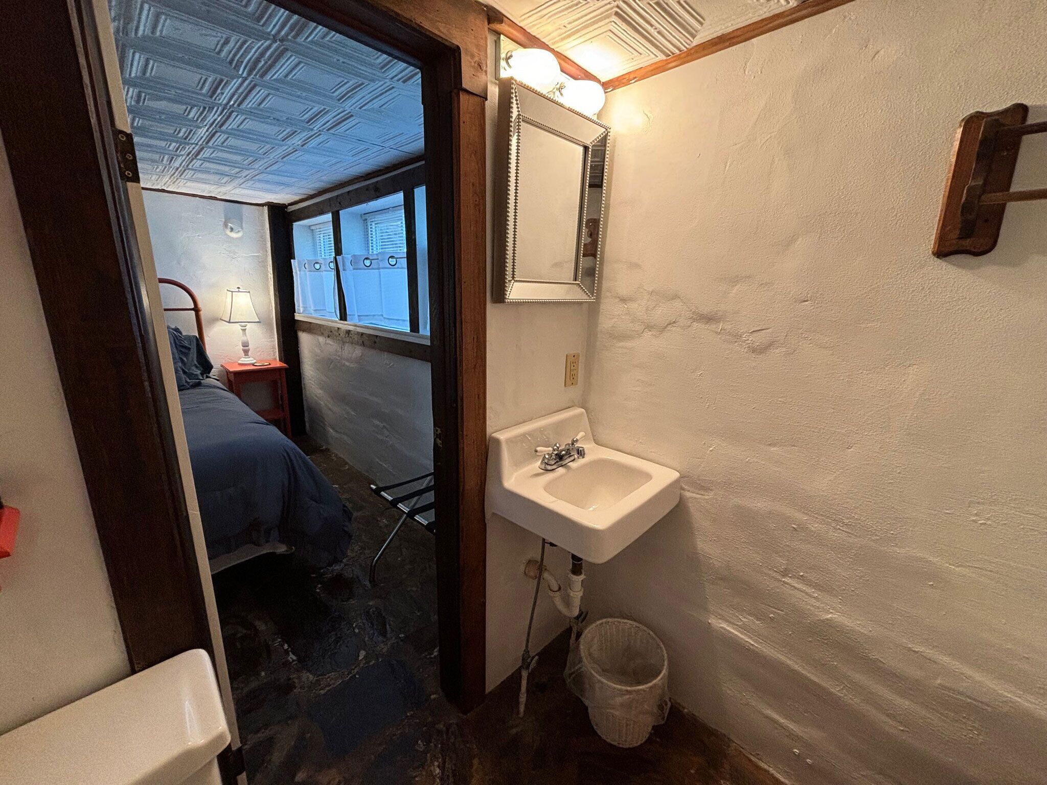 Een kleine, smalle badkamer met een wastafel, spiegel en raam.