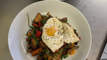 Two white plates with fried eggs and roasted vegetables on a stainless steel table.