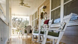 A porch with white rocking chairs, a ceiling fan, and a welcome sign.